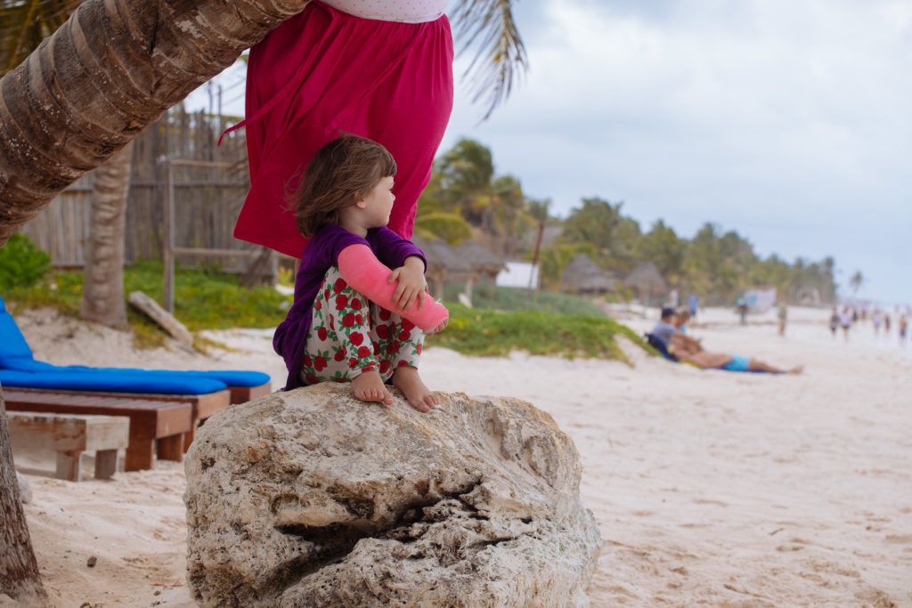 Töchterlein mit rosa Gips unter der schiefen Palme der Playa Xcanan