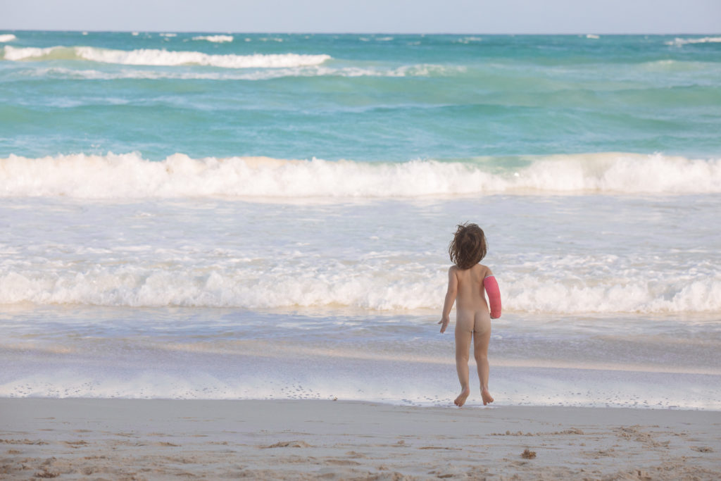 Töchterlein hopst nackig mit Gips vorm karibischen Meer